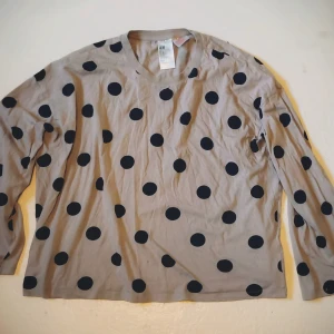 Beige prickig tröja från H&M - Säljer en beige långärmad tröja från H&M med stora svarta prickar. Perfekt för en avslappnad stil. Tröjan har en rund halsringning och är gjord i ett mjukt material. Super mysig tröja att glida omkring som en räkmacka genom livet😜