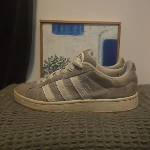 Grå Adidas Campus 00 - Säljer ett par grå Adidas sneakers med klassiska tre ränder i vitt. Skorna har snörning och en gummisula med bra grepp. Går att slänga på me vilken fit som helst. Skorna är i storlek 42 men kan nog passa 41 eller 43. De är väldigt smutsiga men det går att tvätta. Kontakta för fler bilder eller oro 👍