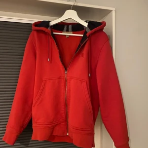 Burberry zip - Säljer en snygg röd huvtröja från Burberry med dragkedja och klassiskt rutigt mönster på insidan av huvan. Den ända bristen är att en del av dragkedjan har lossnat men det påverkar inte funktionen på något sätt. Det kan en skomakare lätt fixa. Står M i tröjan men skulle säga att den sitter mer som S/M. Hör av er vid fler frågor. 