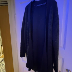 Svart kofta från lager 157 - Säljer en stilren svart kofta från lager 157. Koftan har en öppen design och långa ärmar, perfekt för lager-på-lager under kyligare dagar. Passar både till vardags och mer uppklädda tillfällen.