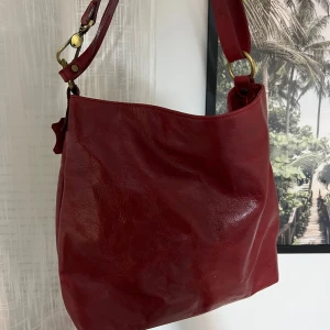 Röd Handväska  - Snygg röd axelväska i äkta skinn från The Trend, tillverkad i Italien. Väskan har en justerbar axelrem och flera praktiska fack med dragkedja inuti 