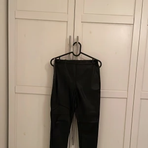 Svarta skinnbyxor med dragkedja - Snygga svarta skinnbyxor med hög midja och dragkedja på sidan. Perfekta för en stilren look med en tight passform. Byxorna är gjorda i ett glansigt material som ger en cool och modern känsla.