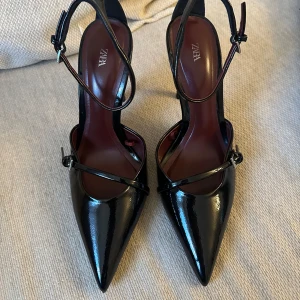 Klackskor - Svarta glansiga klackskor från Zara. Endast använda en gång så skicket är som nytt. Klackhöjd: 10cm. Storlek 38. Nypris: 499kr