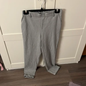 Grå byxor från Vero Moda - Snygga grå byxor från Vero Moda med elastisk midja och svarta ränder längs sidorna. Perfekta för en stilren look. Byxorna har en rak passform och är tillverkade i ett bekvämt material.