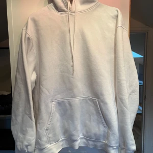 Vit hoodie från HM - Säljer en stilren vit hoodie från HM i storlek M. Den har en klassisk design med en stor ficka framtill och justerbar huva med dragsko. Perfekt för en avslappnad look.
