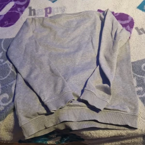 Grå sweatshirt från Lyle & Scott Junior - Säljer en stilren grå sweatshirt från Lyle & Scott Junior. Tröjan har en broderad gul logotyp på bröstet och ribbade muddar vid ärmslut och nederkant. Perfekt för en avslappnad stil.