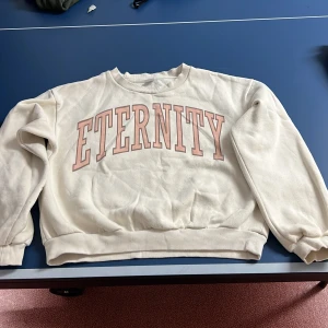 Beige/gul sweatshirt med texten 'Eternity' - Säljer en sweatshirt med texten 'Eternity' i rosa på framsidan. 