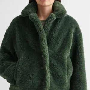 Grön teddyjacka - Mysig grön teddyjacka med knappar framtill. Perfekt för kyliga dagar med sin fluffiga och varma design. Jackan har en avslappnad passform och långa ärmar. Säljer min favvo jacka pågrund av att den inte passar längre.. skriv vid frågor eller fler bilder, inga större defekter💗