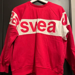 Röd och vit tröja från Svea - Säljer en snygg röd tröja från Svea med deras logga tryckt över bröstet och på baksidan. Tröjan har långa ärmar och en bekväm passform. Fickor i sidan på båda sidorna. Perfekt för en avslappnad stil.