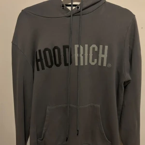 Grå hoodie från Hoodrich - Säljer en stilren grå hoodie från Hoodrich med tryck på framsidan. Den har en justerbar huva med dragsko och en praktisk magficka. Perfekt för en avslappnad look. Finns en liten skada på tröjan bak, men inget som förstör tröjan. Går att diskutera priset 