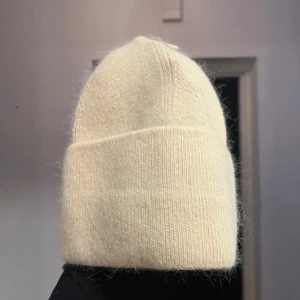 Beige stickad mössa - Snygg och enkel beige stickad mössa som passar perfekt för kyliga dagar. Den har en klassisk design med ribbad kant för extra komfort. Perfekt för både höst och vinter!