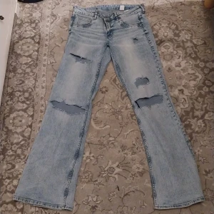 Bootcut jeans i ljusblå denim - Snygga bootcut jeans i ljusblå denim med slitna detaljer. De har en låg midja och klassisk femficksdesign. Perfekta för en avslappnad stil.