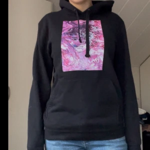 Svart hoodie med rosa tryck  - Snygg svart hoodie med ett abstrakt rosa mönster på bröstet. Den har en justerbar huva med svarta snören och en praktisk magficka. Köpte för några år sen men har aldrig använt så den är som ny, trycket är helt. Från the cool elephant. Original pris ca 500. Strl M men passar S