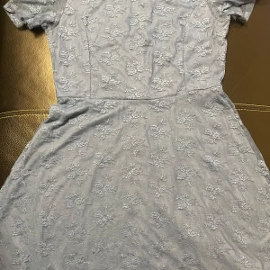 Ljusblå klänning från H&M - Säljer en söt ljusblå klänning från H&M med blommigt mönster. Klänningen har korta ärmar och en rund halsringning. Perfekt för vår och sommar!