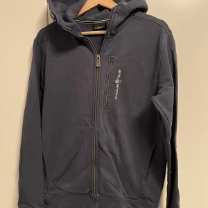 Sail Racing Kofta Storlek Medium  - En mörkblå Sail racing kofta i storlek medium. Koftan är i bra skick förutom att dragkedjan på bröstfickan är trasig. Jag kan tänka mig att justera priset  vid en snabb affär. Tveka inte på att höra av dig om du är intresserad eller om du har några frågor!