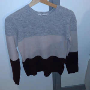 Randig stickad tröja från H&M - Säljer en mysig stickad tröja från H&M i grå, beige och vinröd. Tröjan har ett randigt mönster och långa ärmar, perfekt för kyligare dagar. Den är mjuk och bekväm att bära. Ganska nopprig, därav priset!