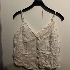 Vit linnetopp från H&M - Säljer en vit linnetopp från H&M med knappar framtill. Toppen har smala axelband och är perfekt för varma dagar. Enkel och stilren design som passar till det mesta.