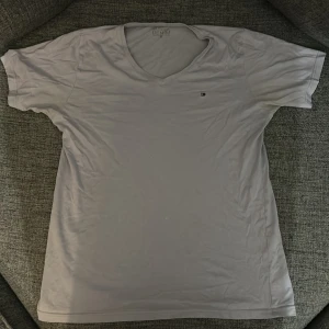 Vit t-shirt från Hilfiger denim - Säljer en klassisk vit t-shirt från Hilfiger Denim med en liten logga på bröstet. T-shirten har en v-ringad hals och korta ärmar. Perfekt för en avslappnad stil.