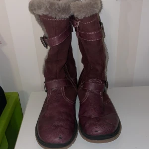 Lila stövlar med pälsfoder - Säljer ett par lila stövlar med mjukt pälsfoder och spänndetaljer st.33.Perfekta för kalla dagar med en robust sula för bra grepp. Stövlarna har en stilren design med dekorativa sömmar.