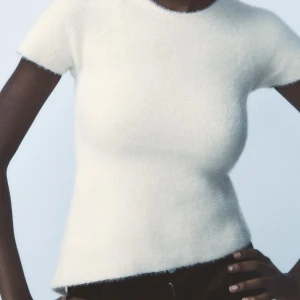 Vit stickad topp med öppen rygg - Säljer en stilren vit stickad topp med korta ärmar och en snygg öppen rygg med knytning. Perfekt för en trendig look! Aldrig använd, bara testad