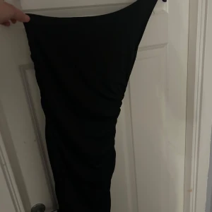 Svart tajt klänning  - Säljer denna svarta klänning då den aldrig används. Den har 1 axelband vilket gör den mycket mer festlig än bara en vanlig klänning.             Vet inte vart den är ifrån då lappen är borta💕