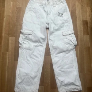 Vita cargobyxor skate jeans Urban Outfitters  - Säljer ett par vita cargobyxor från BDG Urban Outfitters. Byxorna har flera praktiska fickor och en loose passform, perfekt för en avslappnad stil. De är tillverkade i ett slitstarkt material och har en elastisk midja för extra komfort.