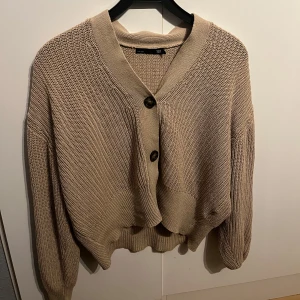 Beige stickad kofta från 157 - Säljer en mysig beige stickad kofta från 157. Koftan har en v-ringad design med stora knappar framtill och långa ärmar. Perfekt för kyliga dagar! Dem sitter även så fint på!!