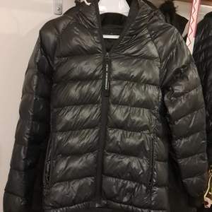 Snygg svart dunjacka från Peak Performance med dragkedja och huva. Perfekt för kyliga dagar med sin quiltade design och långa ärmar. Jackan har en stilren look och är lätt att matcha med olika outfits.