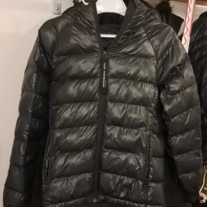 Svart dunjacka från Peak Performance - Snygg svart dunjacka från Peak Performance med dragkedja och huva. Perfekt för kyliga dagar med sin quiltade design och långa ärmar. Jackan har en stilren look och är lätt att matcha med olika outfits.