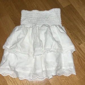 Vit kjol från H&M - Charmig vit kjol från H&M med broderade detaljer och volanger. Kjolen har en elastisk midja för bekväm passform och är tillverkad i 100% bomull, vilket gör den perfekt för varma dagar. Även bra att köpa sommarklöder i tid ❤️storlek 158 men skulle säga att den passar xs-xxs 