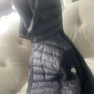 Moncler cardigan  - Säljer en snygg svart dunjacka från Moncler med stickade detaljer och dragkedja. Perfekt för kyliga dagar med sin quiltade design och långa ärmar. Jackan har en stilren look och är tillverkad i högkvalitativt material.