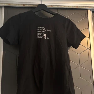 Svart t-shirt med tryck - Snygg svart t-shirt med vitt tryck på bröstet som säger 'Developing Scandinavian design since 1997'. Perfekt för en stilren och minimalistisk look. T-shirten har korta ärmar och en klassisk rund halsringning.