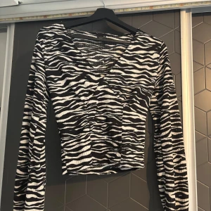 Zebramönstrad ribbad topp - Säljer en cool zebramönstrad topp med ribbad struktur. Den har en v-ringad design och långa ärmar, perfekt för att sticka ut i mängden. Passar bra till både jeans och kjol!