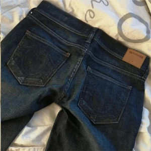 Mörkblå jeans från True Religion - Snygga mörkblå jeans från True Religion i modellen Cora Straight. Low waisted och perfekta för en stilren look. Midjemått är 38 cm och innebenslängd 86 cm. Tryck på köp nu!