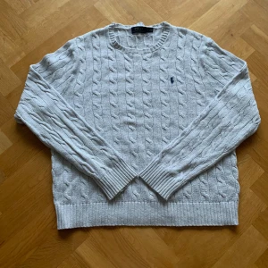 Grå kabelstickad tröja från Ralph Lauren - Skit snygg och skön Ralph lauren sweater. Grå färg med svart logga. Använd lite men inga tecken på slitningar eller skador. Storlek L. Modellen på bilden är 185 och väger 83kg. Priset kan diskuteras.