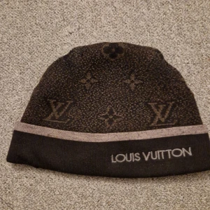 Svarta mössa  -  Mössan har en diskret rand i beige och märkesnamnet broderat framtill. Perfekt för att hålla stilen under kyliga dagar.