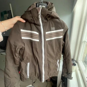 Brun jacka från Helly Hansen - Säljer en brun jacka från Helly Hansen med vita detaljer och dragkedja. Jackan har en huva och två fickor med dragkedjor. Perfekt för kyligare väder med sin funktionella design. Sååå fin älskar den men säljer då jag hittat en ny som passar mig bättre, pris kan diskuteras vid snabba köp!