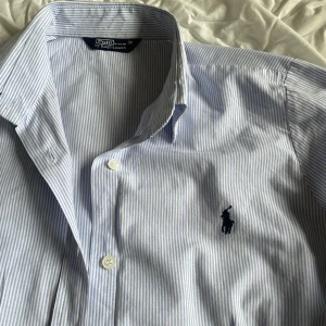 Blå- och vitrandig skjorta från Ralph Lauren - PRIS KAN DISKUTERAS❤️ Säljer en klassisk blå- och vitrandig skjorta från Polo Ralph Lauren. Skjortan har långa ärmar och knappar framtill. Den ikoniska loggan är broderad på bröstet. Perfekt för en stilren och vintage look. 