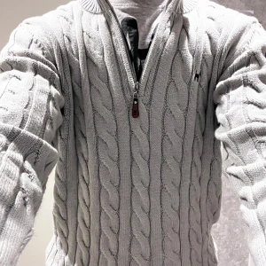 Williot half zip grå - Säljer en stilren grå kabelstickad tröja från Morris. Tröjan har en halv dragkedja och ett diskret broderat emblem på bröstet. Perfekt för kyligare dagar med sin ribbade krage och muddar.