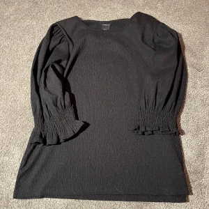 Svart klänning från Lindex - Snygg svart blus från Lindex med trekvartsärmar och smockdetaljer vid ärmsluten. 