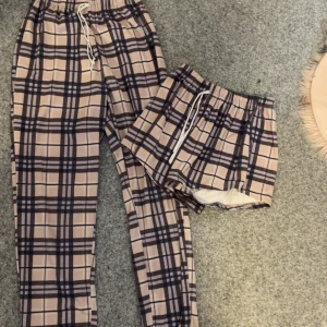 Rutig pyjamasbyxa och shorts - Säljer ett set med rutig pyjamasbyxa och matchande shorts. Båda plaggen har elastisk midja med snörning för extra komfort. Perfekt för en avslappnad dag hemma.