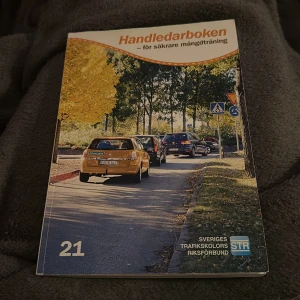 Handledarboken - för säkrare mängdträning - Handledarboken är en guide för säkrare mängdträning, utgiven av Sveriges Trafikskolors Riksförbund. Omslaget visar en bilkö på en väg kantad av träd i höstfärger. Perfekt för den som vill bli en bättre handledare i trafiken.