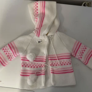 Vit och rosa stickad kofta med huva - Söt vit stickad babykofta storlek 68 med rosa ränder och mönster. Den har en huva och knytband med tofsar framtill. Perfekt för att hålla sig varm.