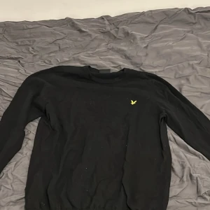 Svart tröja från Lyle & Scott - Säljer en stilren svart tröja från Lyle & Scott med deras ikoniska gula logotyp på bröstet. Tröjan har långa ärmar och är perfekt för en avslappnad stil. Passar bra till både jeans och chinos.