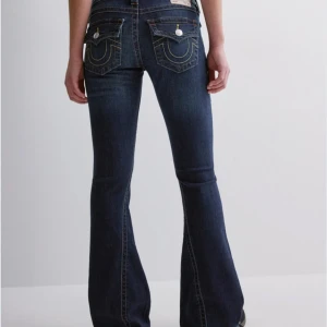 Mörkblå jeans från True Religion - Snygga mörkblå jeans från True Religion med låg midja och utsvängda ben. De har dekorativa sömmar och knappar på bakfickorna. Perfekta för en avslappnad stil.