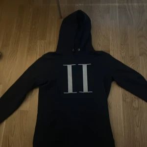 Les duex hoodie saknar snöret storlek S - Säljer en svart hoodie med ett stilrent tryck av två romerska siffror på framsidan. Tröjan har en klassisk design med huva och långa ärmar. Perfekt för en avslappnad stil.