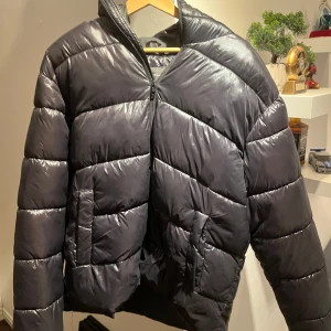 Svart pufferjacka - En lite tunnare glansig dunjacka som är perfekt nu till våren. Jackan är bara använd några gånger och är i mycket bra skick. Storlek L.