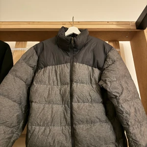 Jacka, nuptse, The North Face - Säljer en grå dunjacka från The North Face med svarta detaljer. Jackan har en dragkedja framtill och är perfekt för kyligare väder. Storlek L