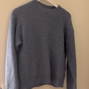 Blå stickad tröja - Säljer en mysig blå stickad tröja från H&M. Tröjan har en rund halsringning och långa ärmar, perfekt för kyligare dagar. Den är enkel och stilren, vilket gör den lätt att matcha med olika outfits. Perfekt för höst och vinter!