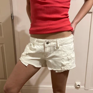 Vita jeansshorts - Snygga vita jeansshorts med fransiga kanter och slitna detaljer. Perfekta för en avslappnad sommarlook. De har en knapp och dragkedja framtill samt klassiska fem fickor.